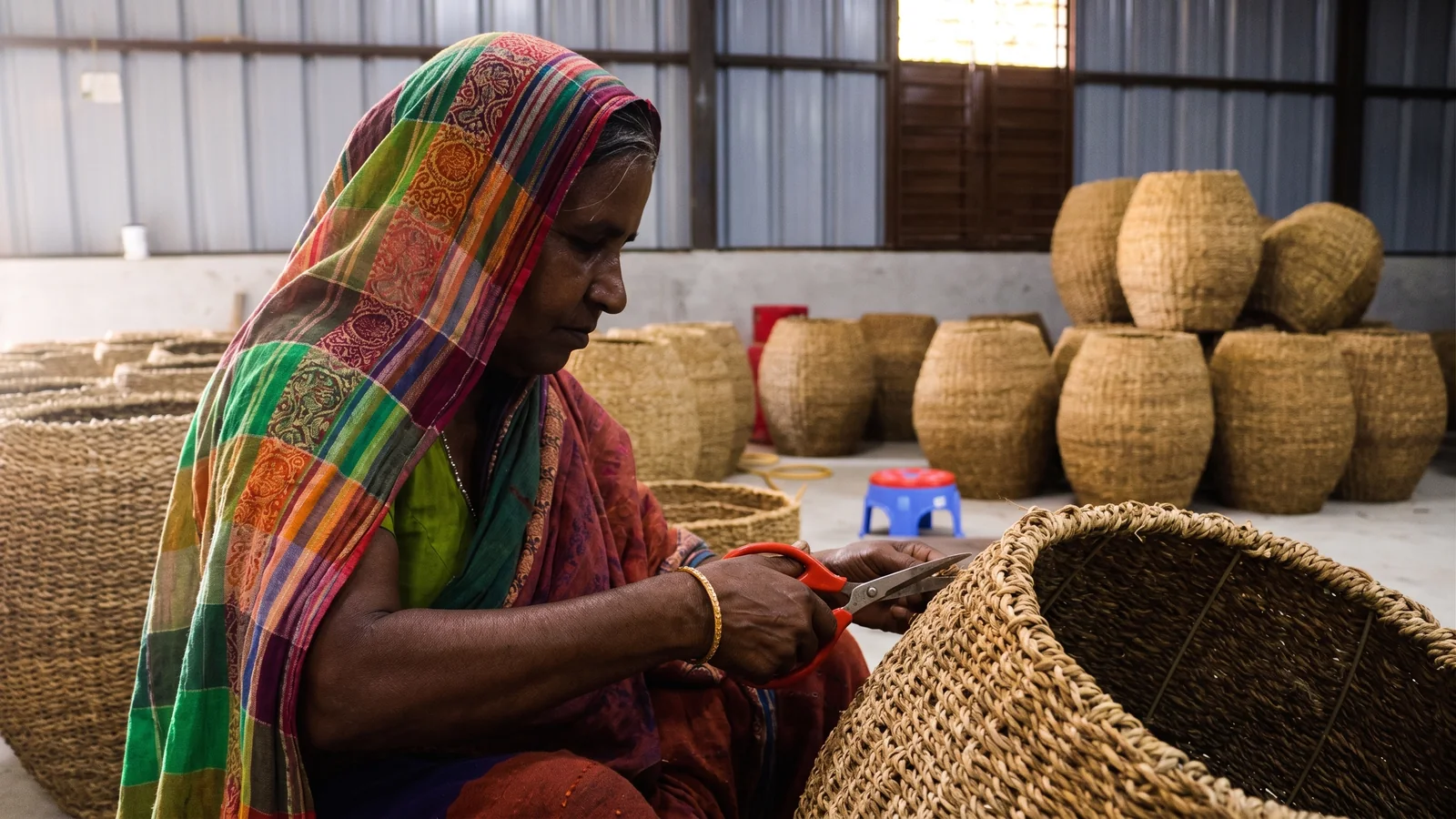 A woman trimming the rim of a finished jute basket