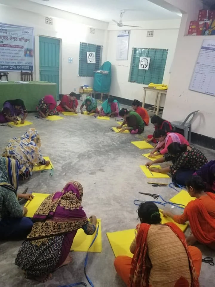 Trainees seated on the floor, cutting and measuring yellow cloth