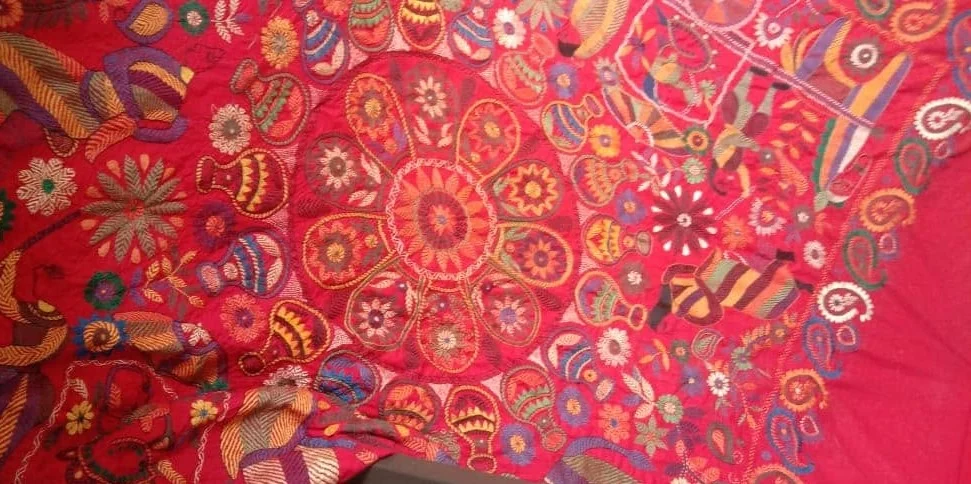 A red nakshi kantha cloth with a hand-embroidered floral medallion at its centre
