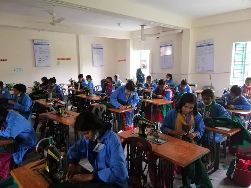 Trainees seated at treadle sewing machines during a tailoring course