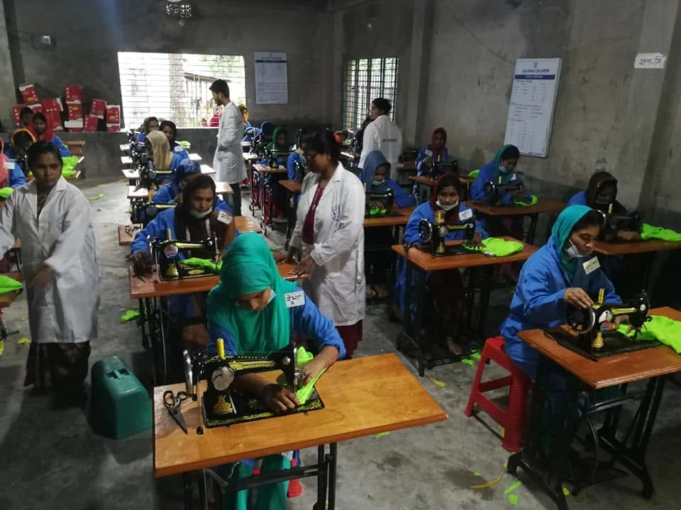 Instructors in white coats guiding trainees at their sewing machines
