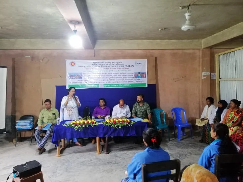 A trainer addressing seated trainees at a sewing workshop