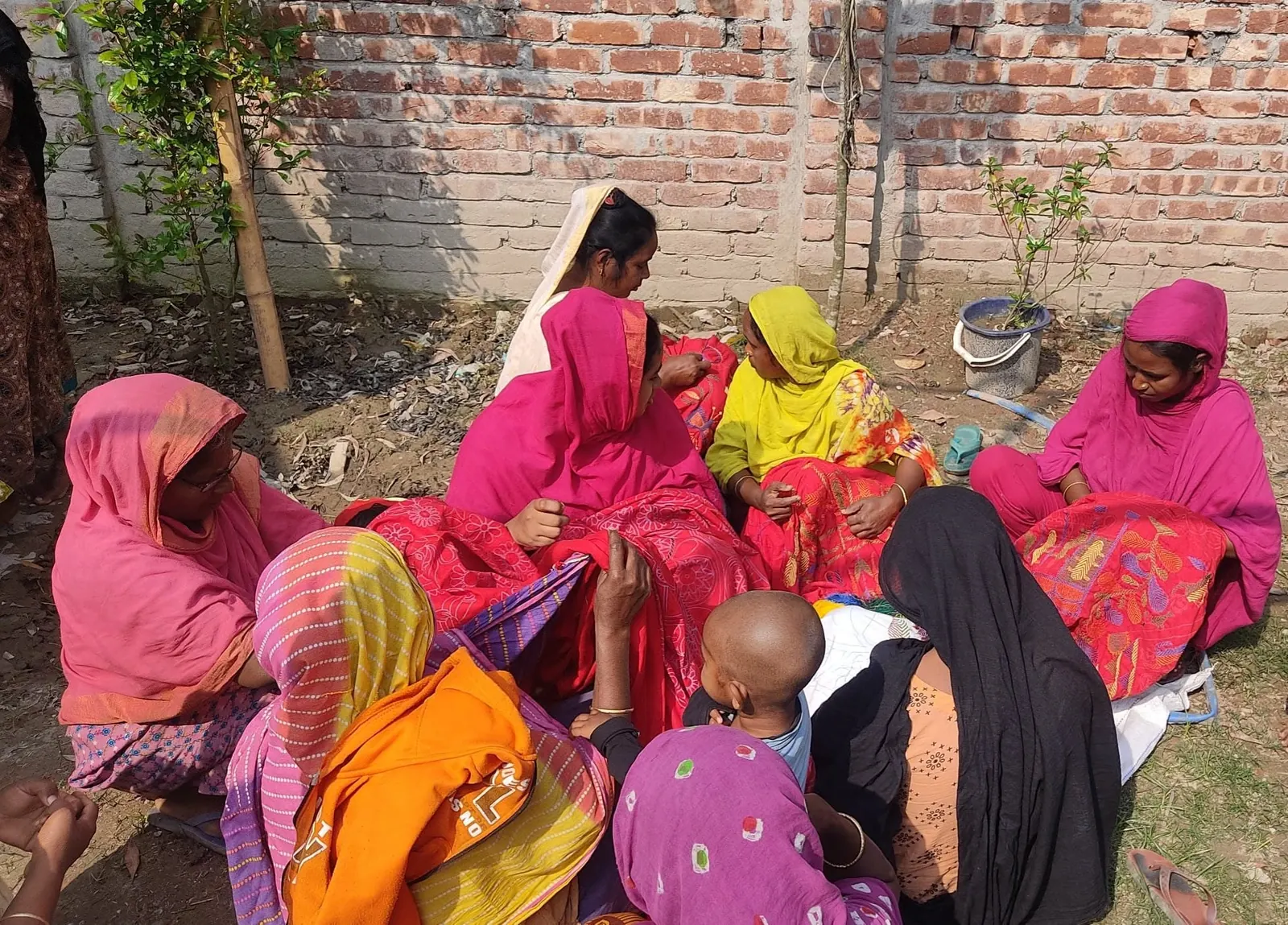 Members of the samity sitting together in the yard, hand-stitching kantha cloth