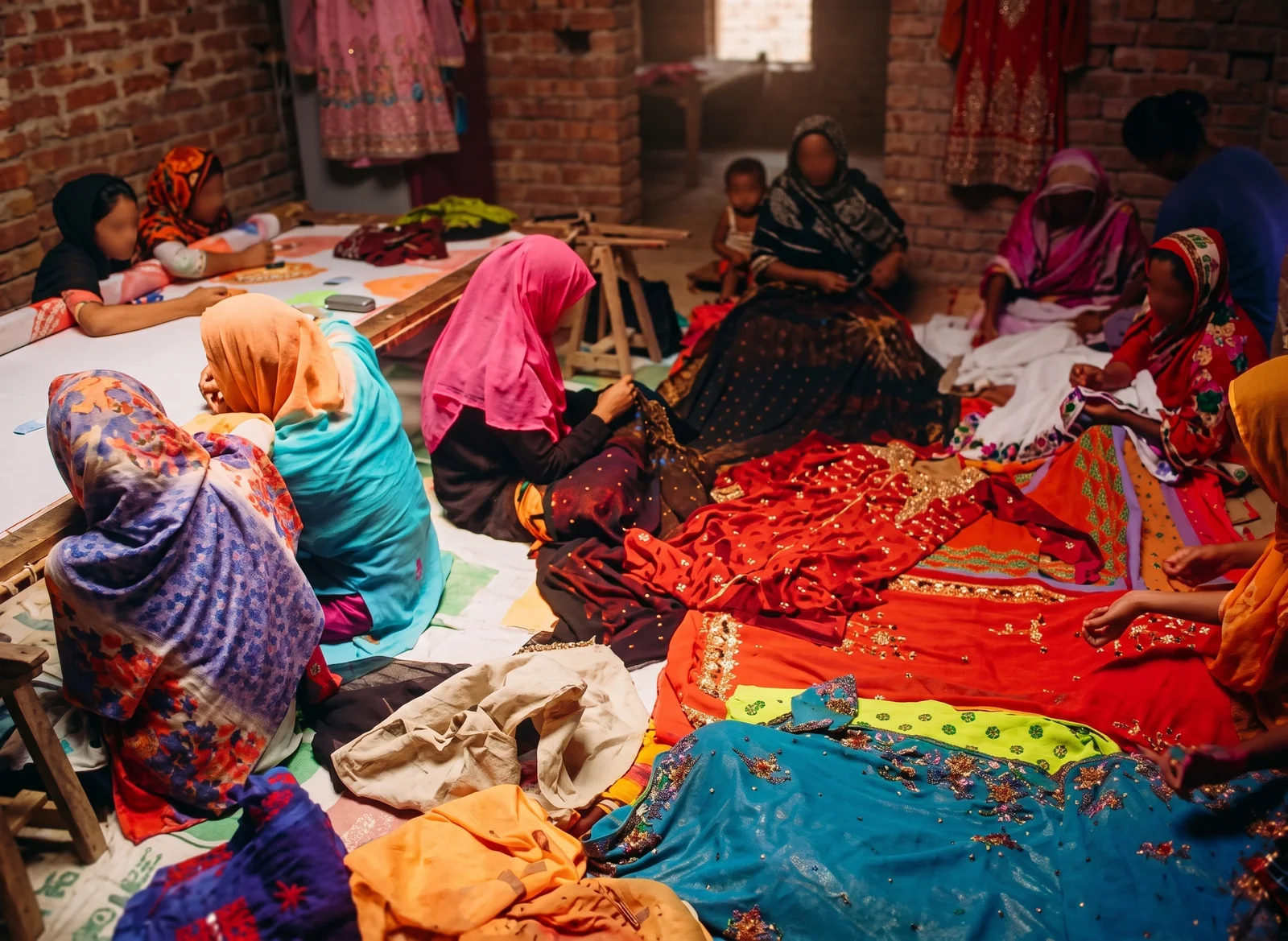 Women sitting together and hand-stitching bright cloth in the workroom